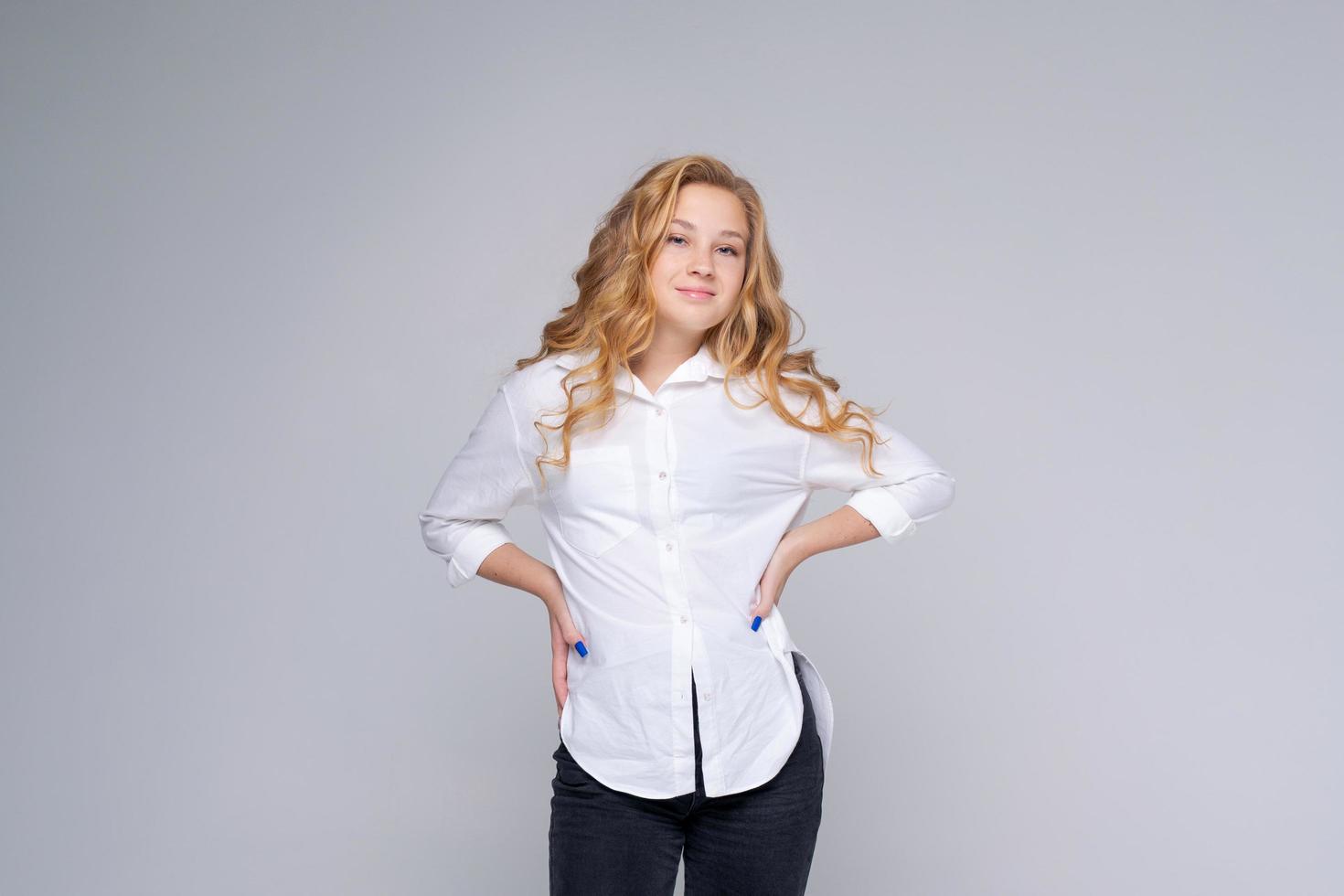 Smiling young blonde woman in white shirt posing isolated on gray walls photo