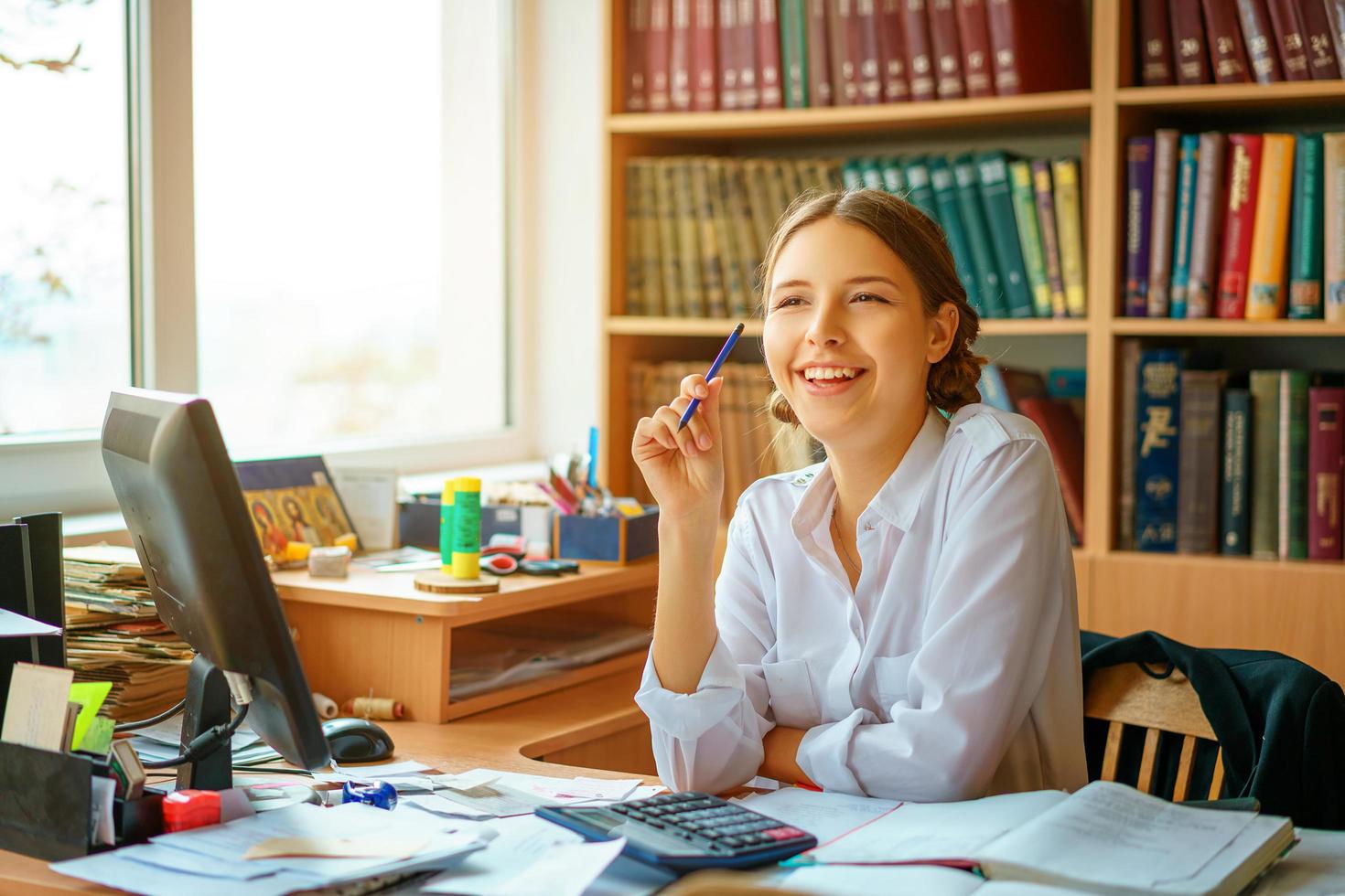 young happy business lady in white shirt sitting at table with computer and papers working environment photo