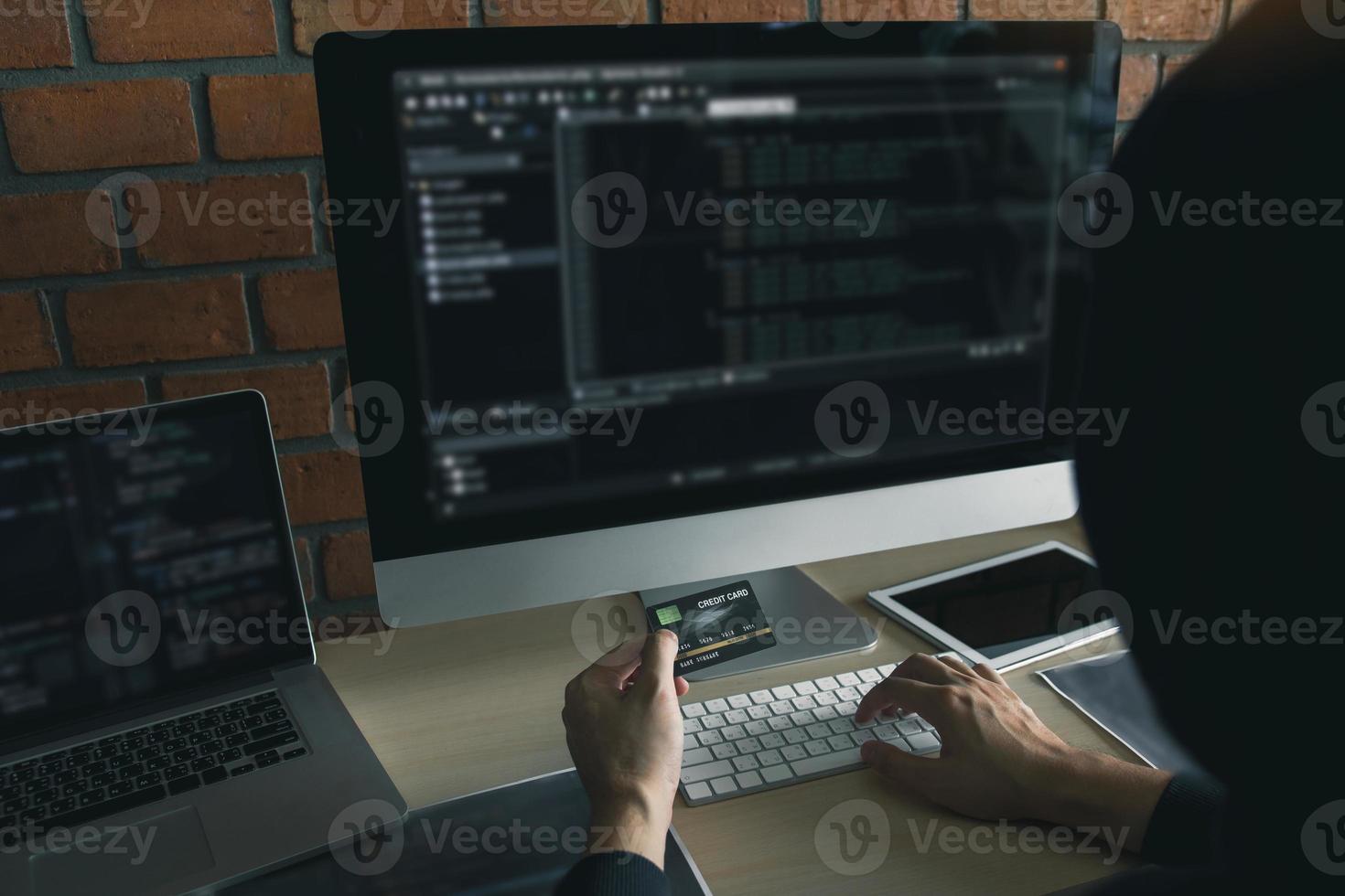 Hacker in the hood working with computer and holding credit card with payment hacking concept. photo