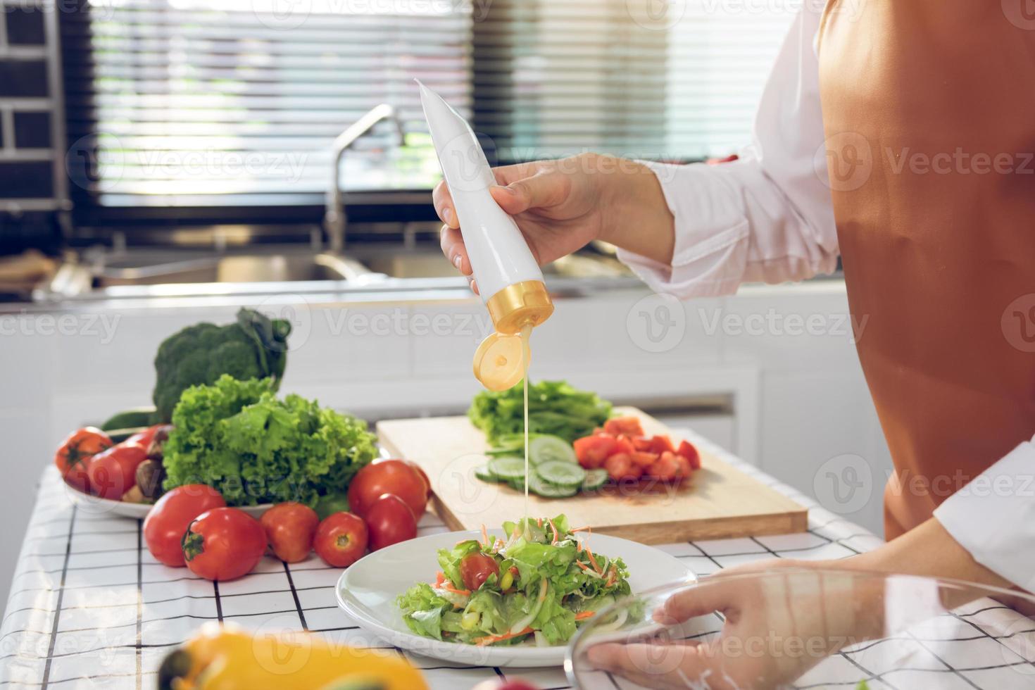 Asian woman squeezes mayonnaise on a salad plate at the kitchen cooking table. photo