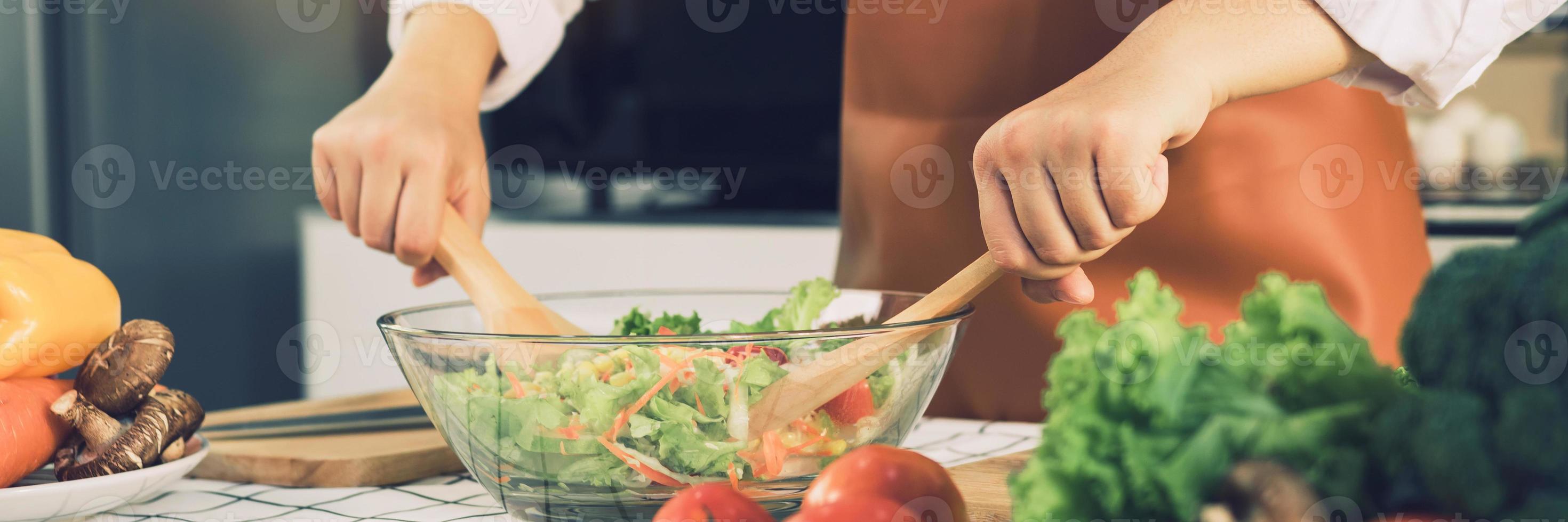 Asian woman is mixing the ingredients in a salad bowl at the kitchen cooking table. photo