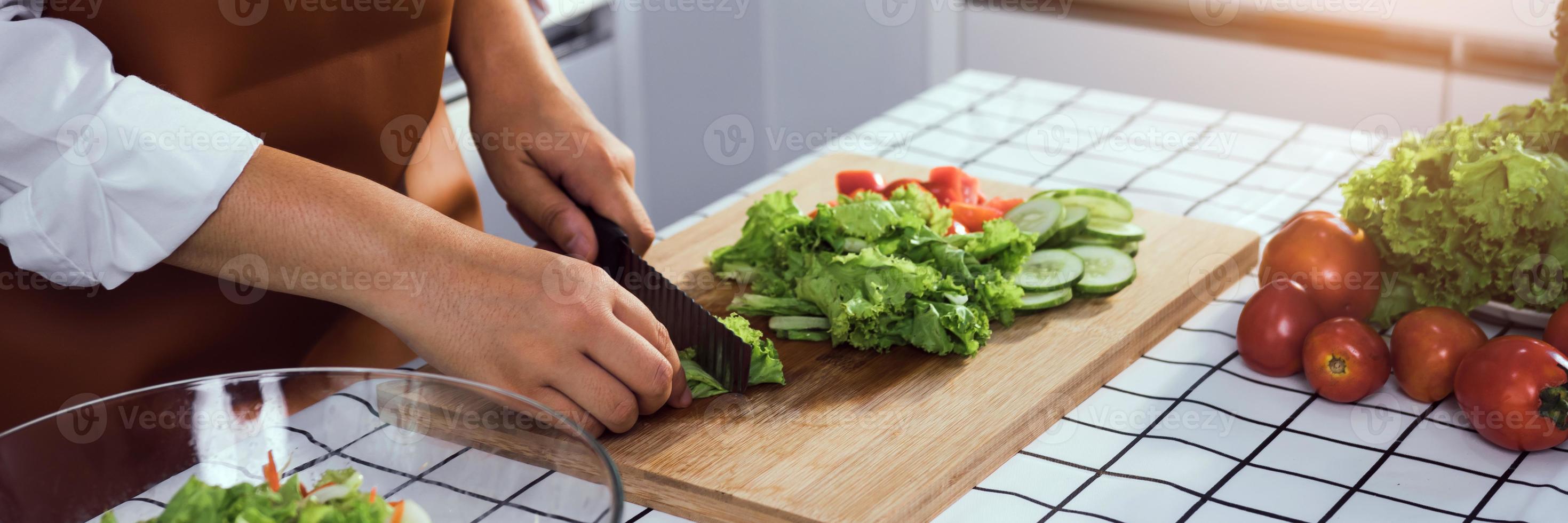 Asian woman uses a knife to cut the salad greens in the kitchen. photo