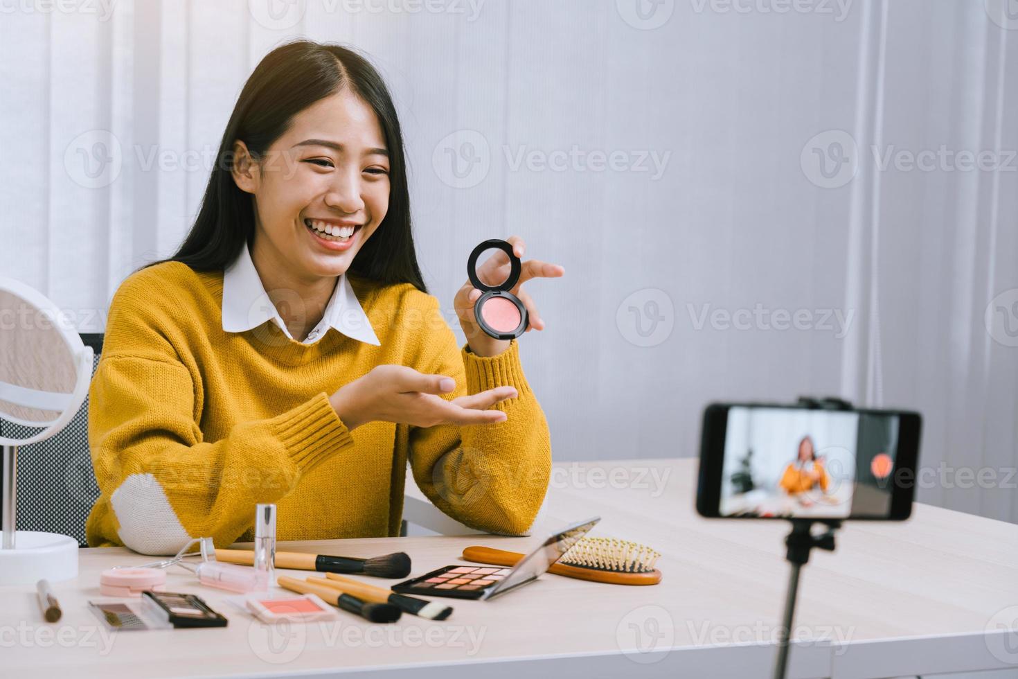 Beautiful asian woman blogger using camera phone recording vlog video live streaming and showing how to make up cosmetics at home. photo