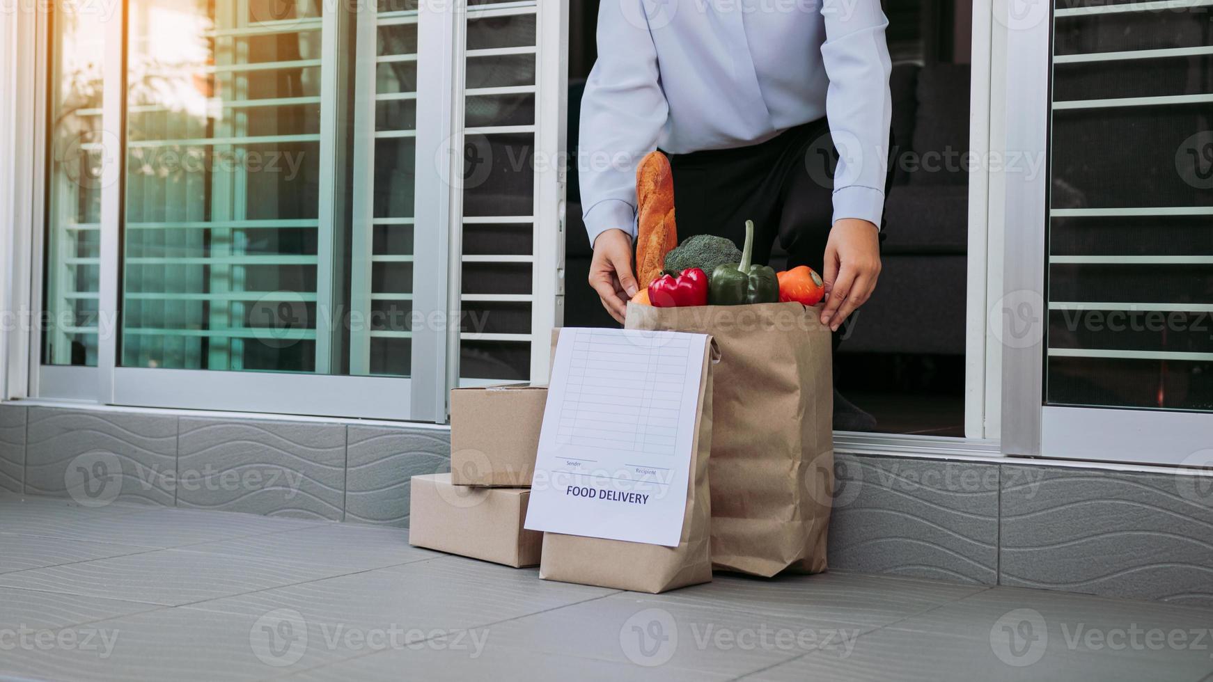 Asian woman open the door and took the bag of food ordered by the carrier to put in front of the house to prevent the epidemic. photo