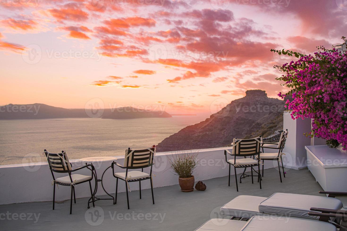 Beautiful view of Caldera and enjoying romantic scenery sunset Aegean sea, Santorini. Couple travel vacation, honeymoon destination. Romance with flowers, two chairs table and sea view. Luxury holiday photo