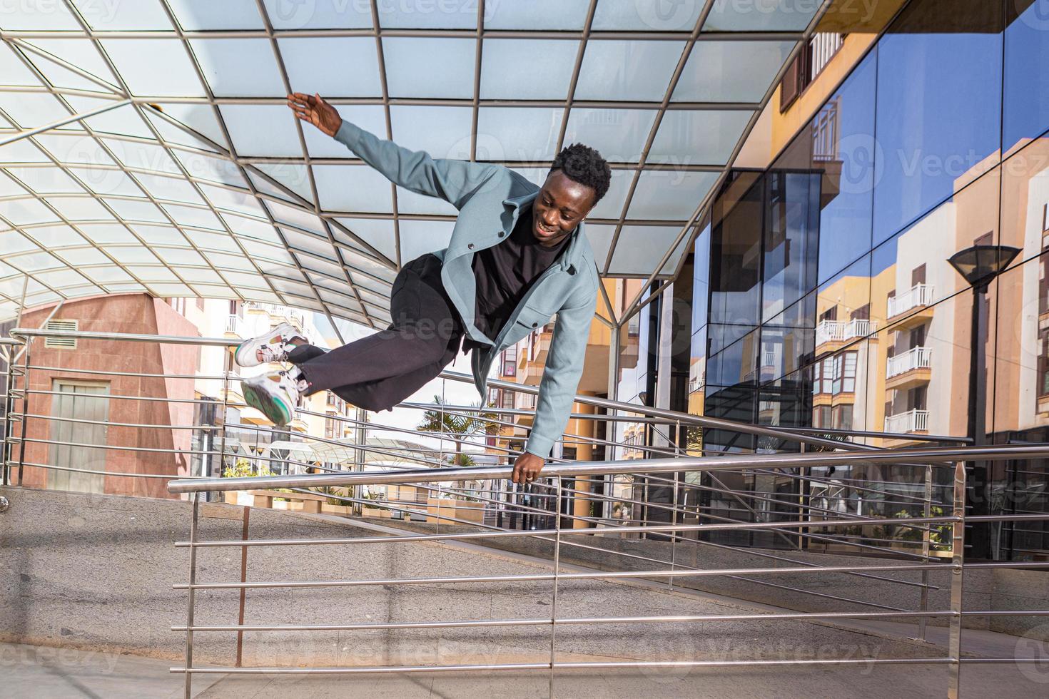 Happy black male millennial jumping over railing near modern building photo