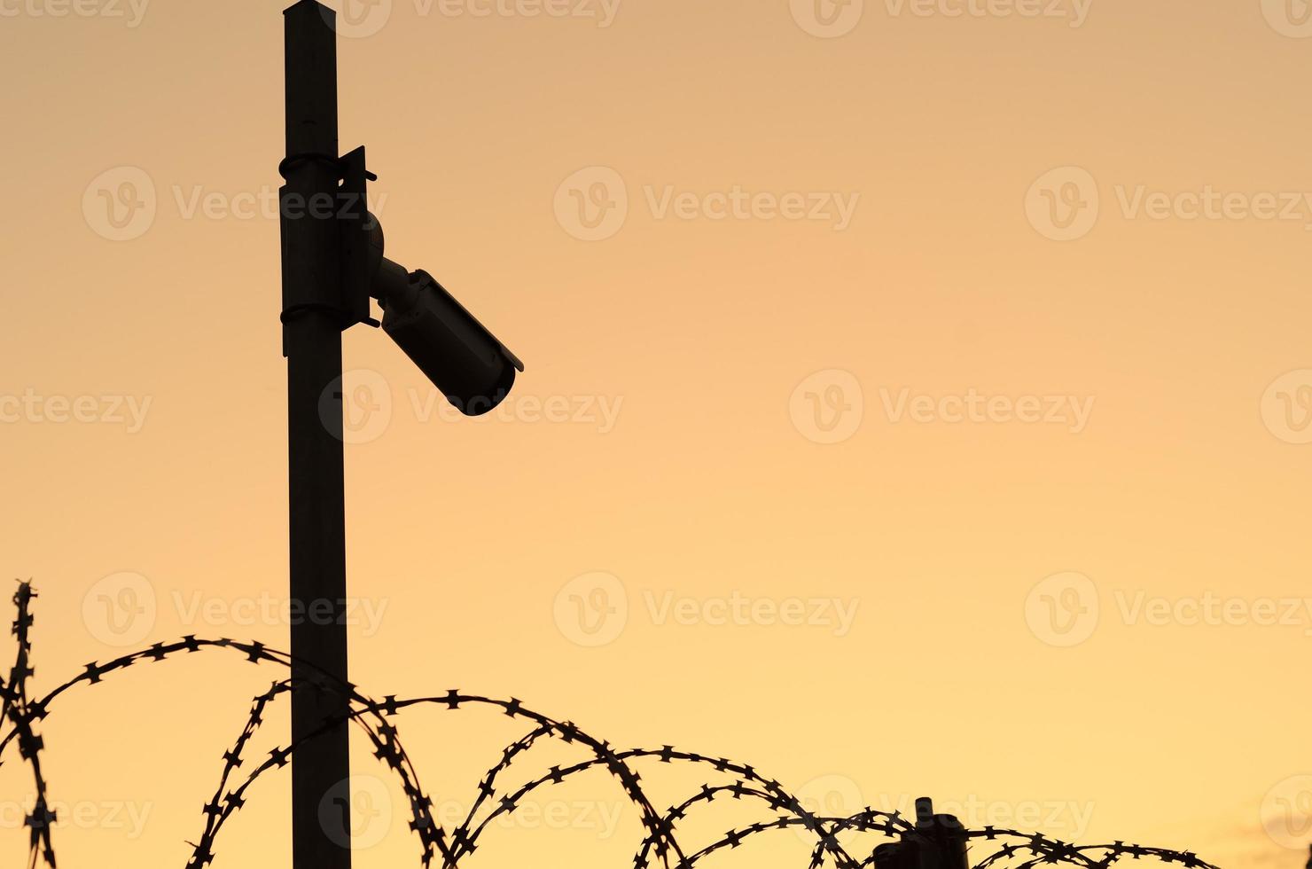 silueta de la cámara de seguridad en el poste al atardecer. observación del perímetro del área protegida con alambre de púas. espacio para texto. foto