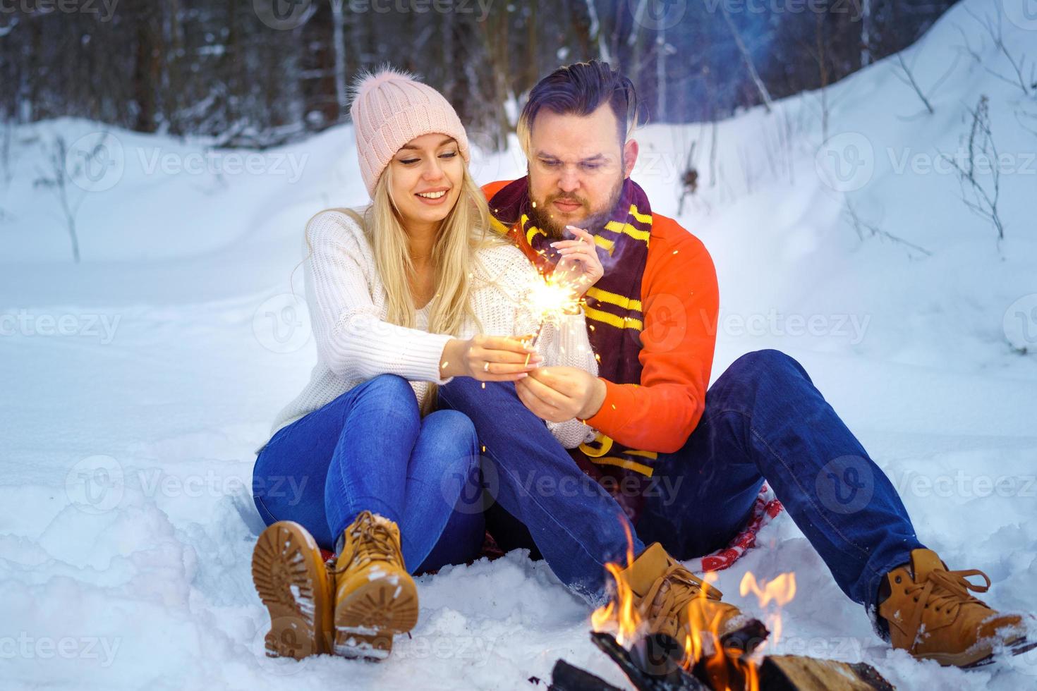 Happy couple in winter in the forest by the fire with sparklers photo