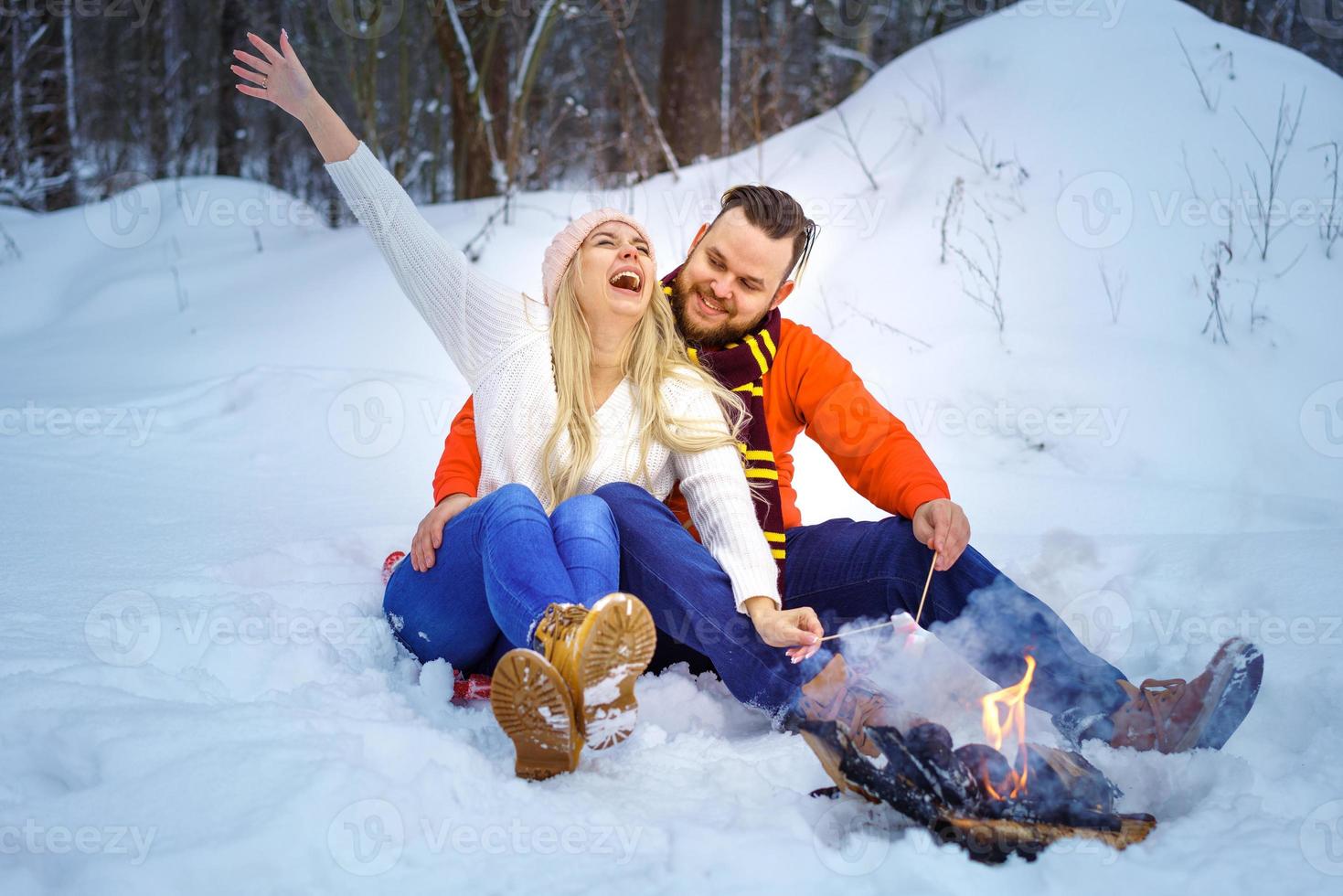 happy couple man and woman in winter in the forest fry marshmallows on the fire photo