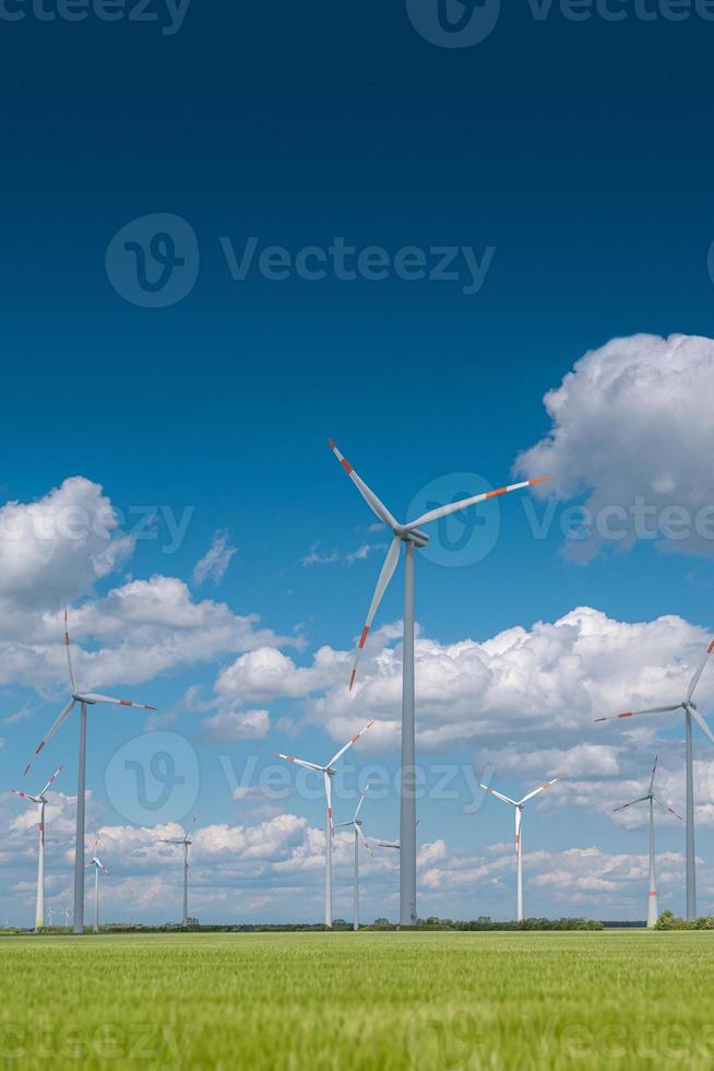 View over beautiful farm landscape with green wheat field and wind turbines to produce green energy in Germany, Spring, blue dramatic rainy sky and sunny day. photo