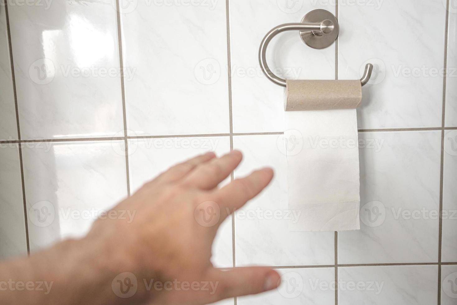 Man hand is trying to take last piece of toilet paper roll in the bathroom, closeup, details. photo