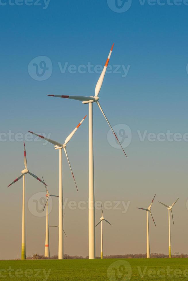 Group of big wind turbines to generate electrical power, green ecofriendly energy at blue sky with sunset warm colors in Europe. Concept of green sustainable energy production. photo