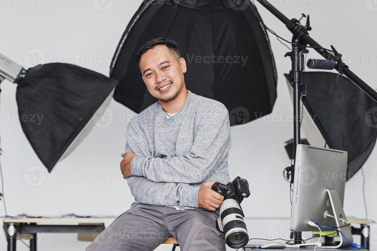 Asian photographer sitting and holding camera with confidence smile photo