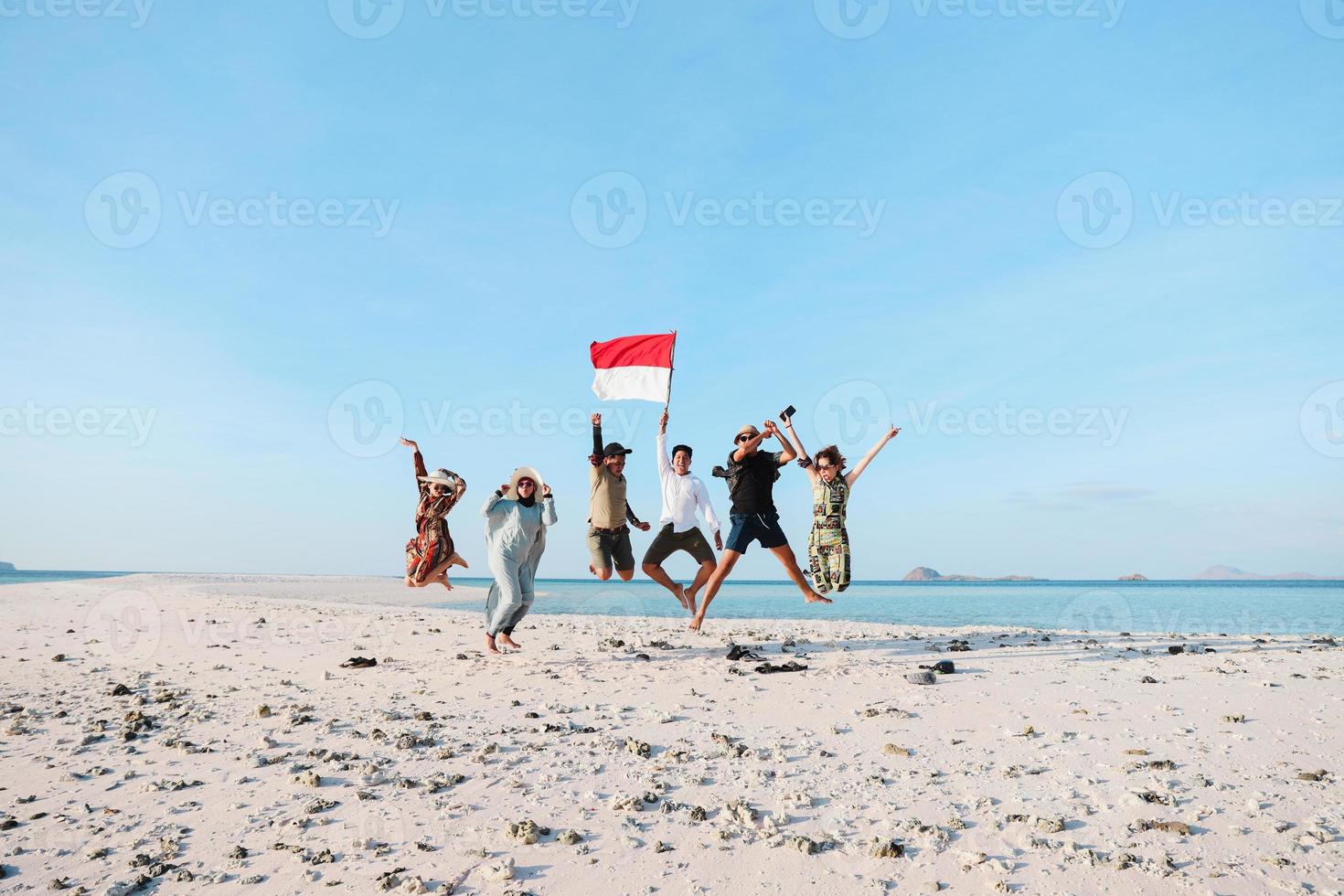 Group of people jumping on the beach with a man holding Indonesian flag photo