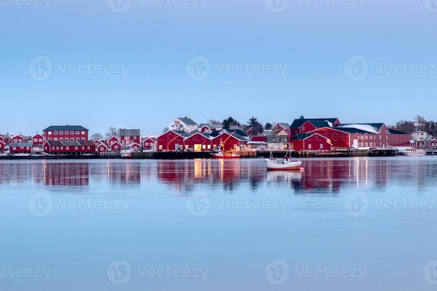 Red fishing warehouse with fishing boat reflection on coastline photo