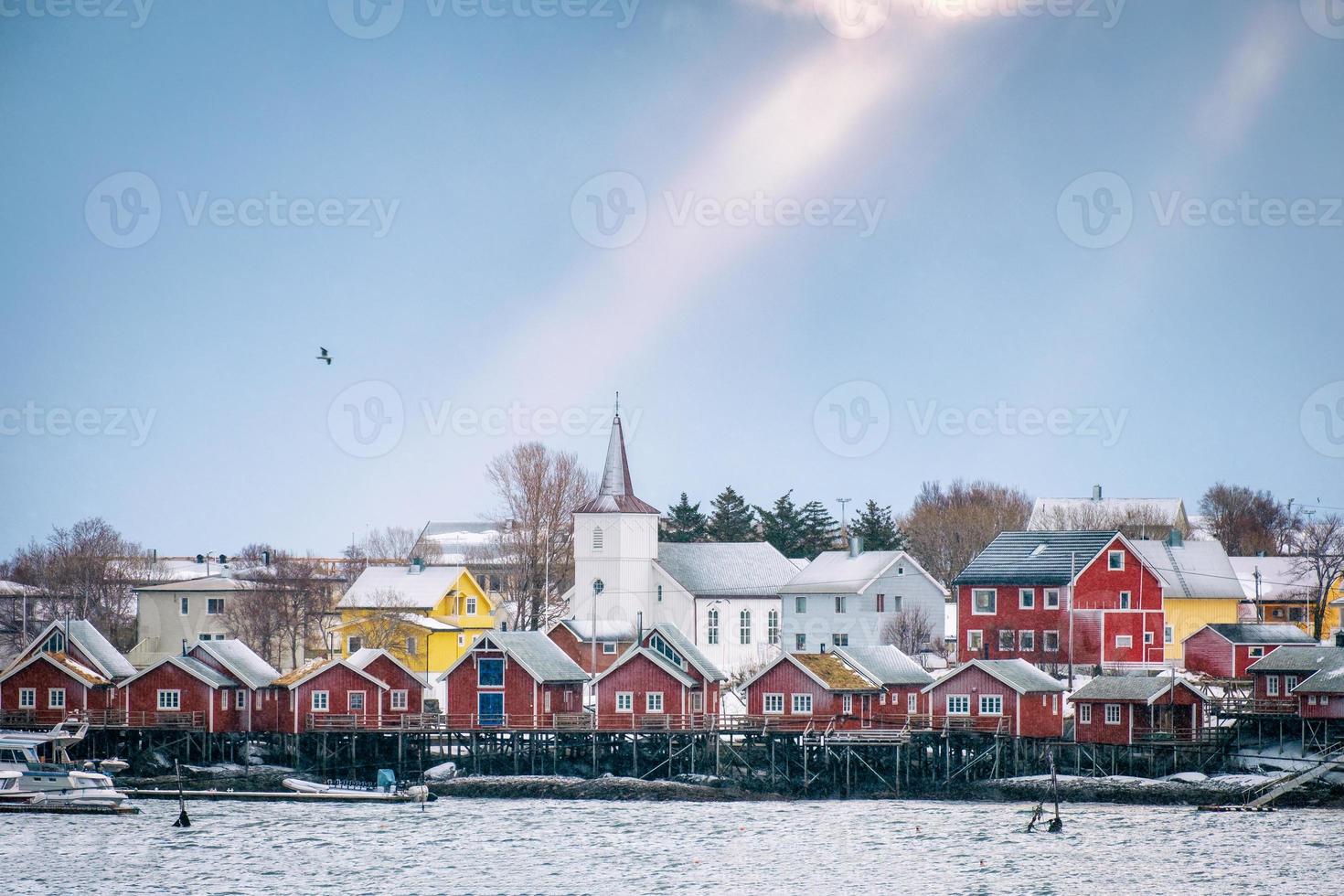 Christian church on fishing village at coastline with sunlight beaming in blue sky photo