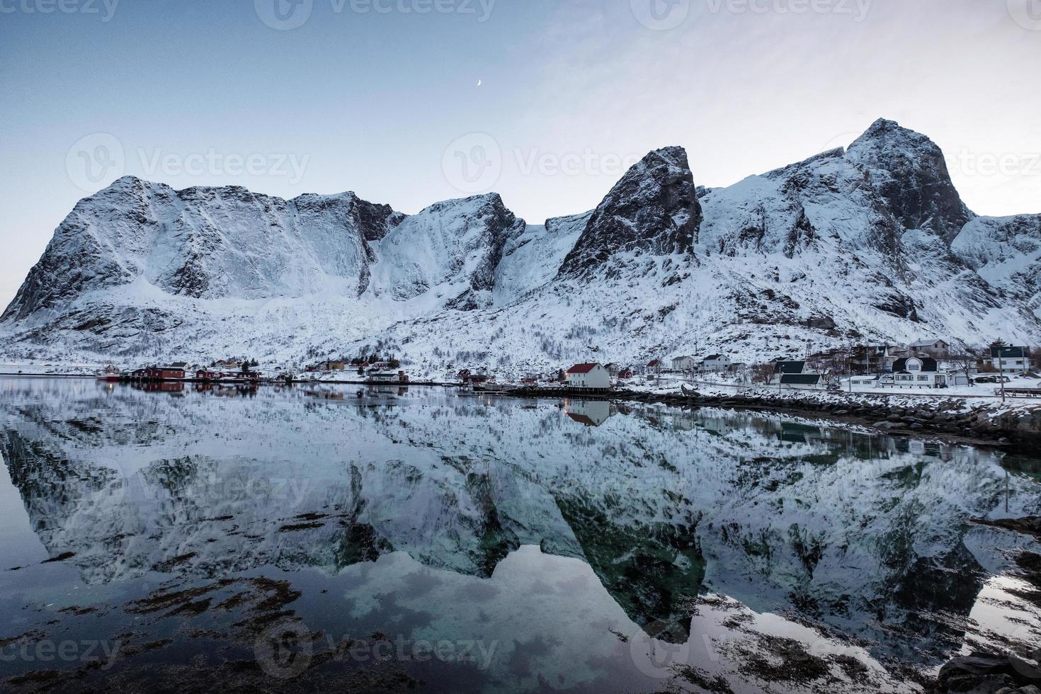 Cordillera nevada con reflejo de rorbuer escandinavo en la costa de Lofoten foto