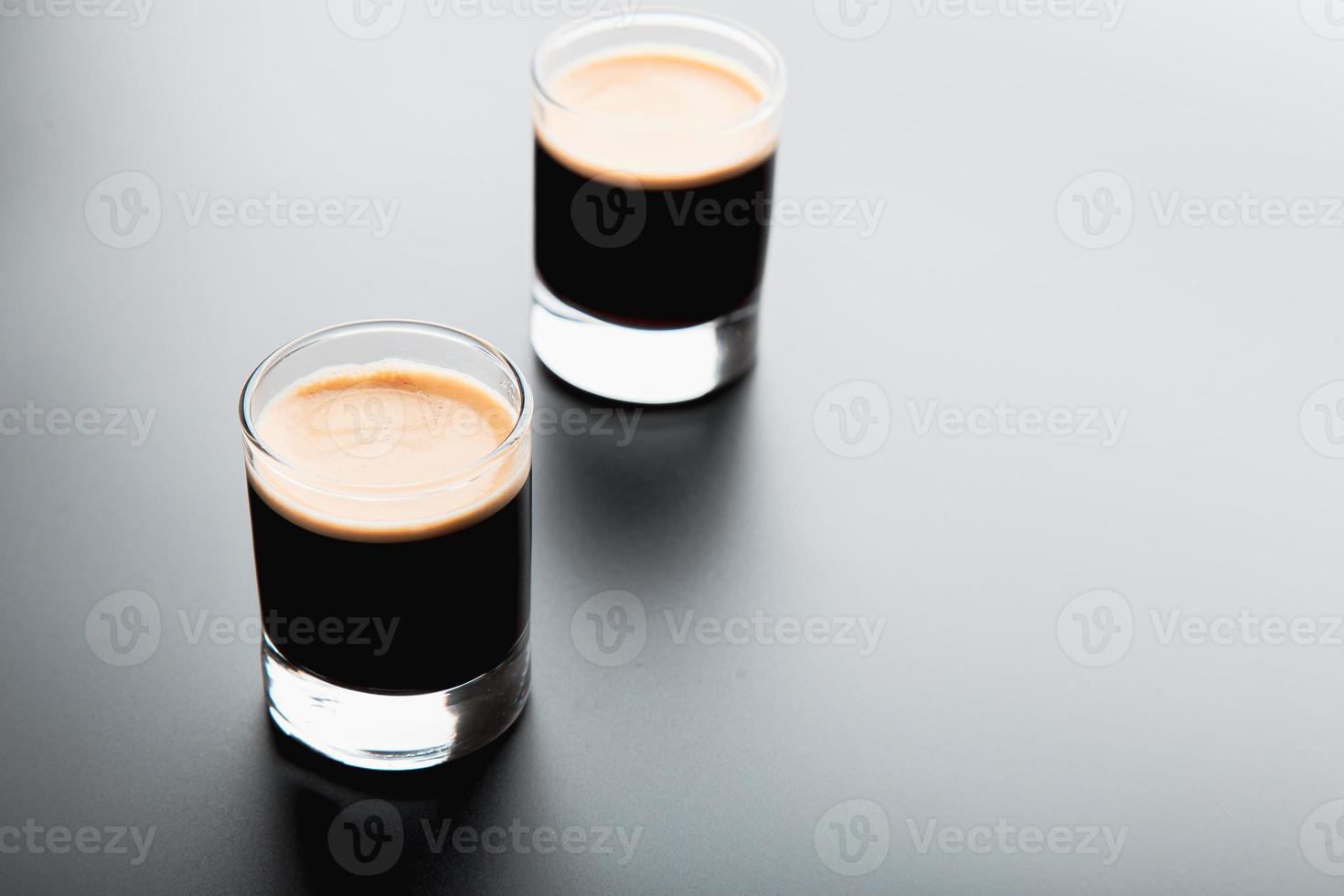 Vista detallada de primer plano de dos vasos de chupito espresso sobre un fondo negro brillante y elegante con espacio para copiar. foto