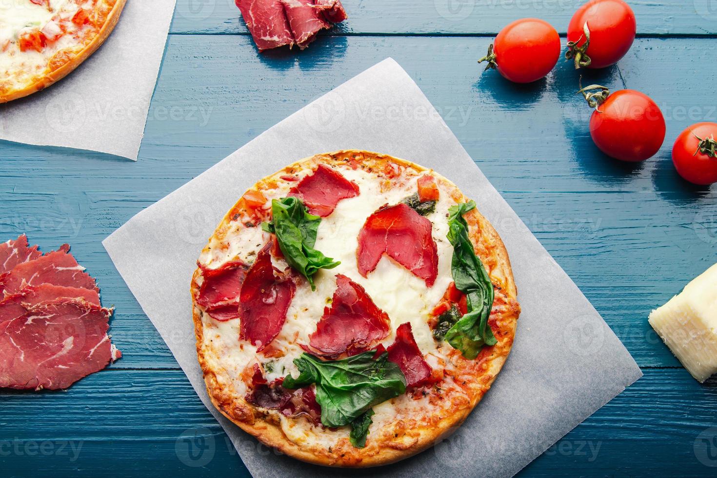 Flat lay view of pizza over trendy blue wooden vintage backdrop with pizza ingredients. photo