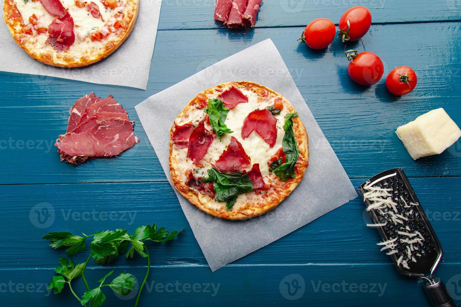 Flat lay view of pizza over trendy blue wooden vintage backdrop with pizza ingredients. photo