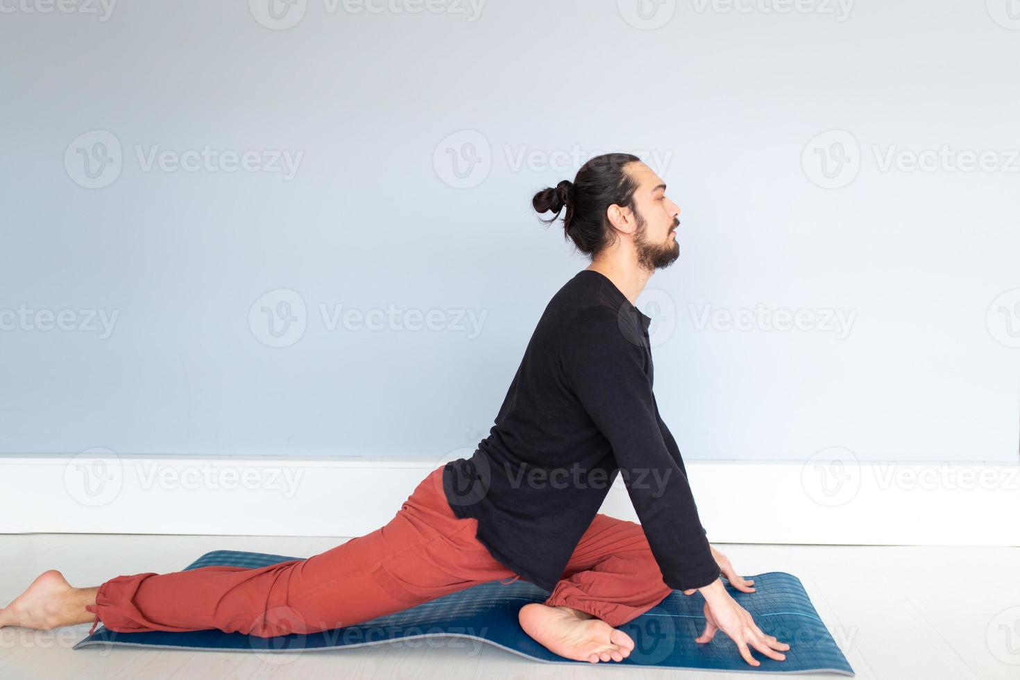 Young Caucasian long haired white man is performing yoga in a studio or house. photo