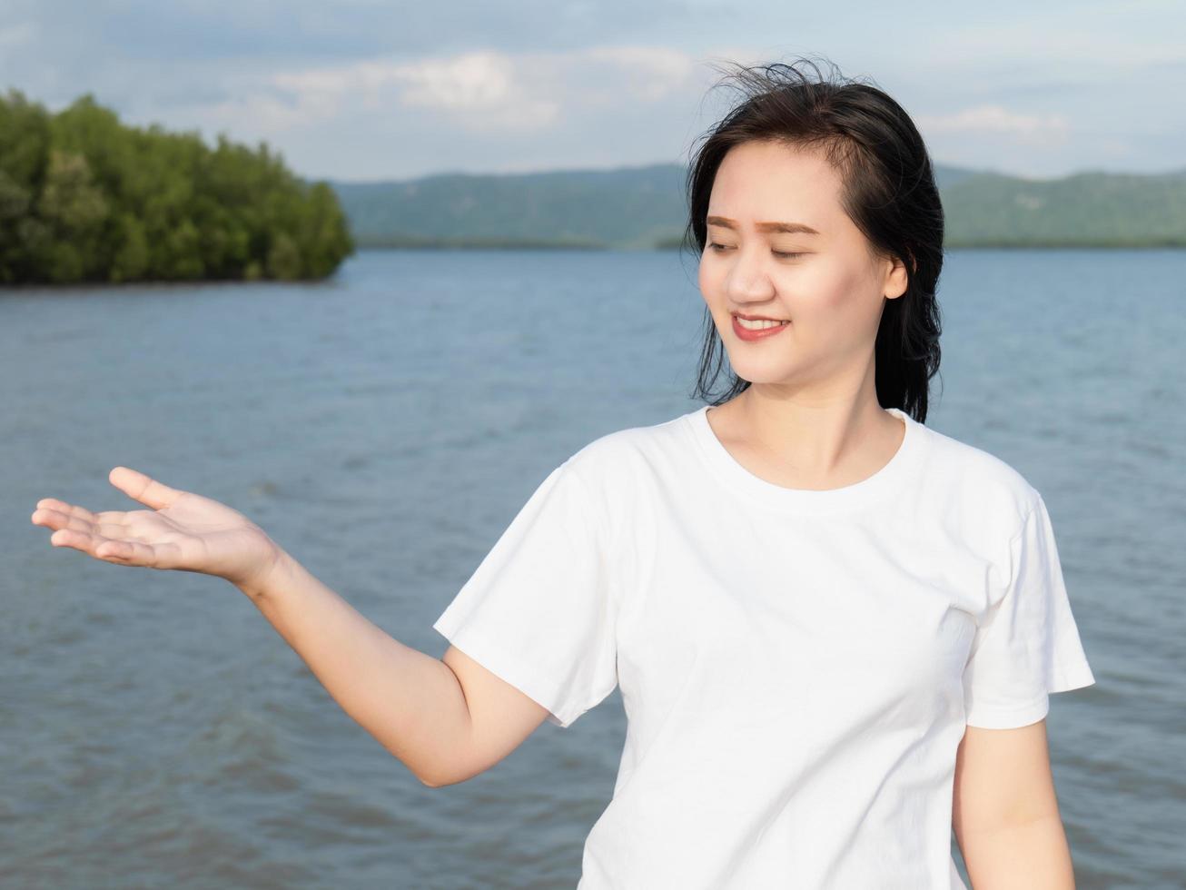 una chica asiática con camisa blanca sonriendo pone las manos boca abajo para tomar la brisa fresca que sopla y desafía la brisa marina y la luz del sol. el día que ella salió de vacaciones foto