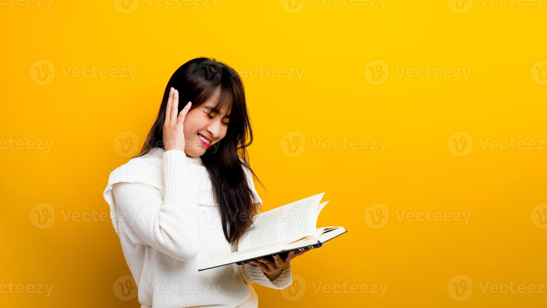 foto de una niña asiática sonriendo mientras lee un libro mientras sonríe sobre un fondo amarillo concepto de lectura de libros una niña a la que le encanta leer libros