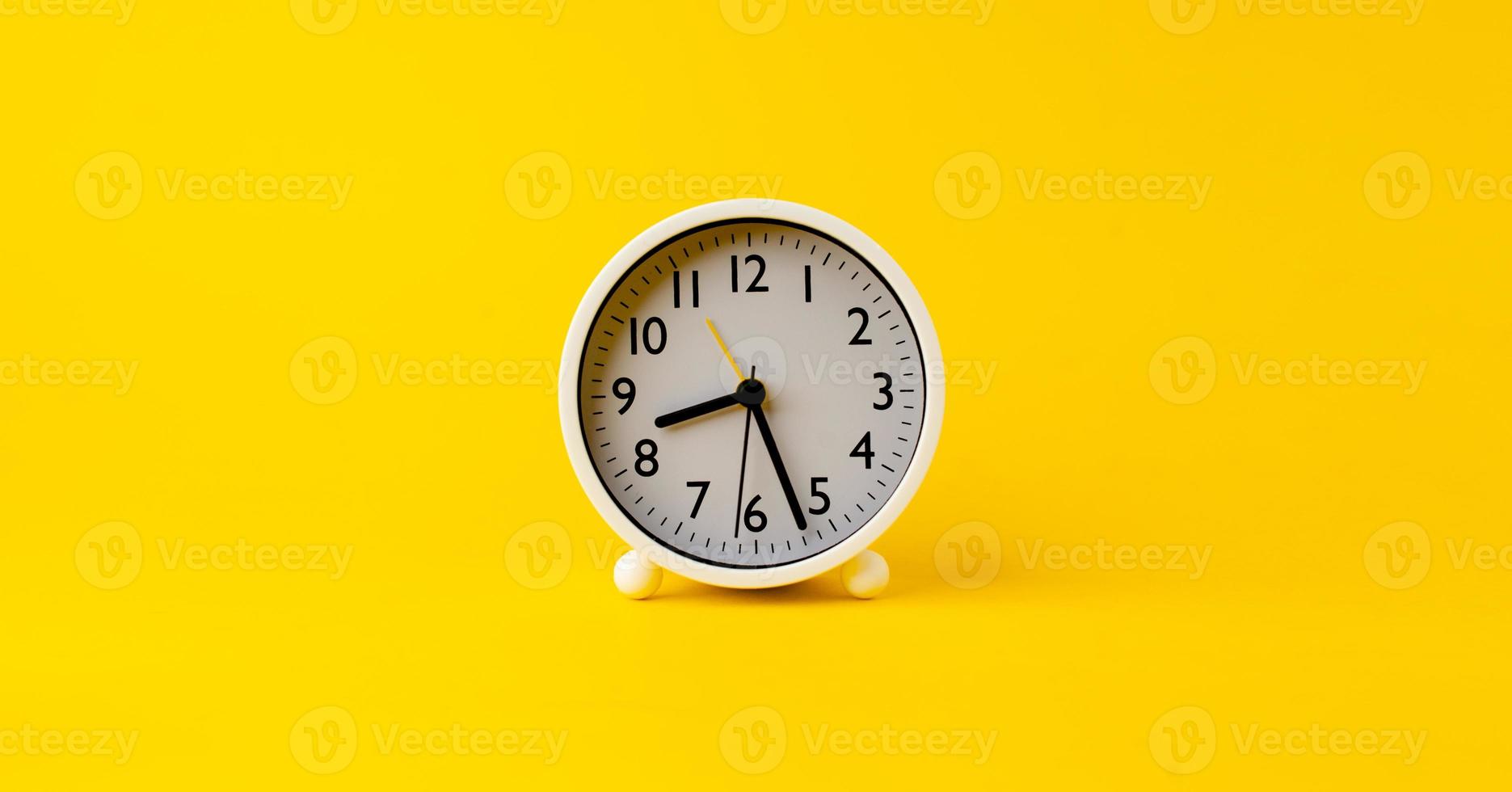 despertador blanco el reloj indica la hora de despertarse por la mañana. colocado sobre un fondo amarillo foto