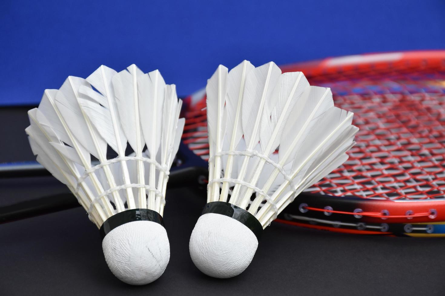 Cream white badminton shuttlecock and racket with neon light shading on green floor in indoor badminton court, blurred badminton background, copy space. photo