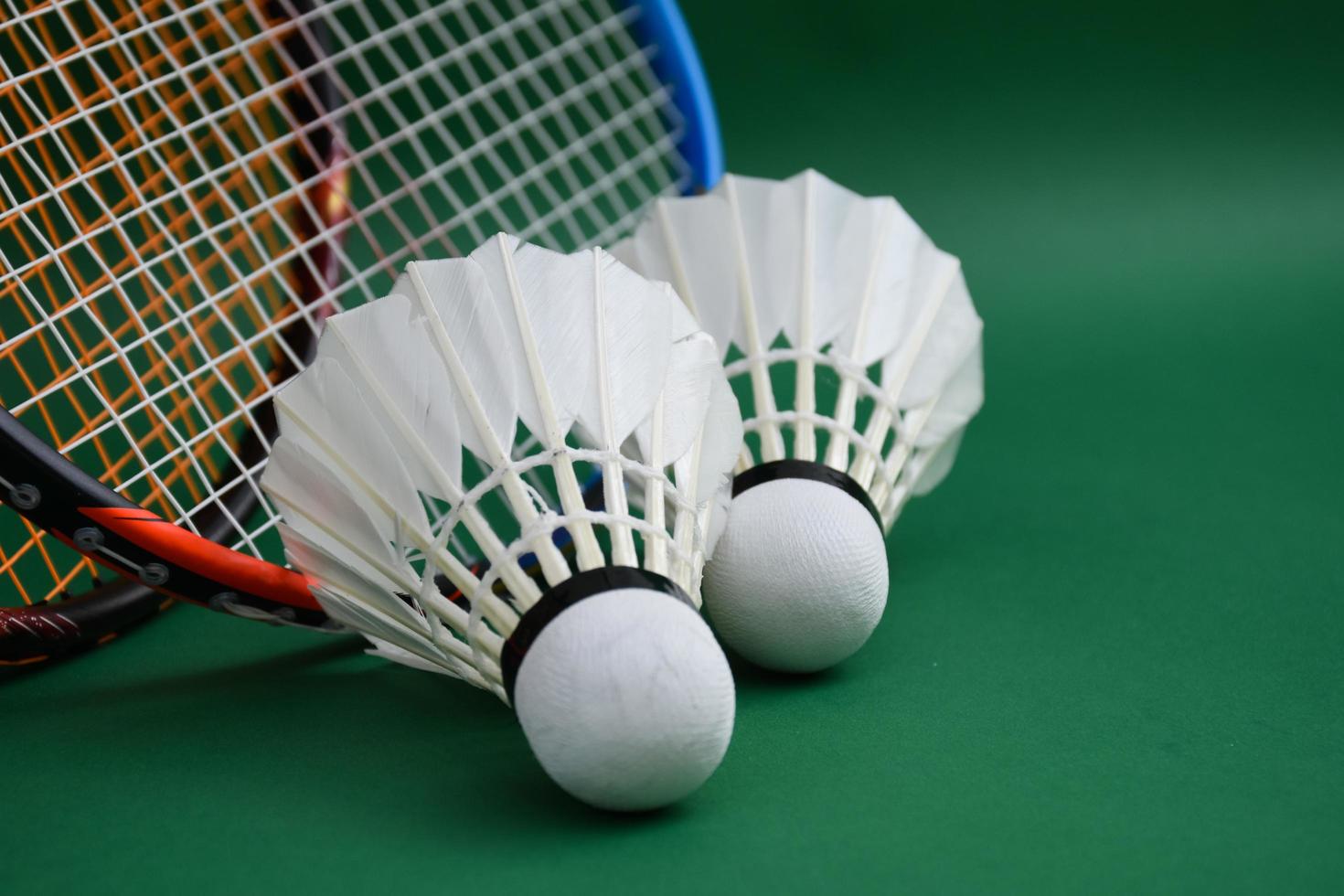 Cream white badminton shuttlecock and racket with neon light shading on green floor in indoor badminton court, blurred badminton background, copy space. photo