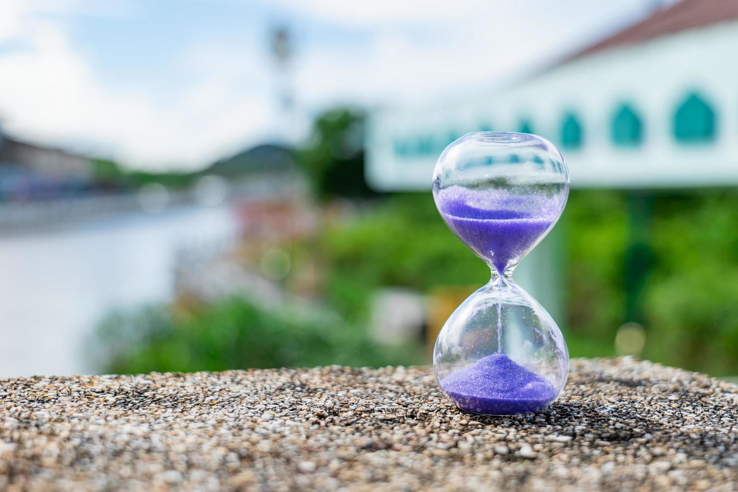 el reloj de arena estaba sobre la áspera superficie rocosa cerca del canal de la marea creciente. muestra que el agua que fluye nunca retrocede. el tiempo también foto