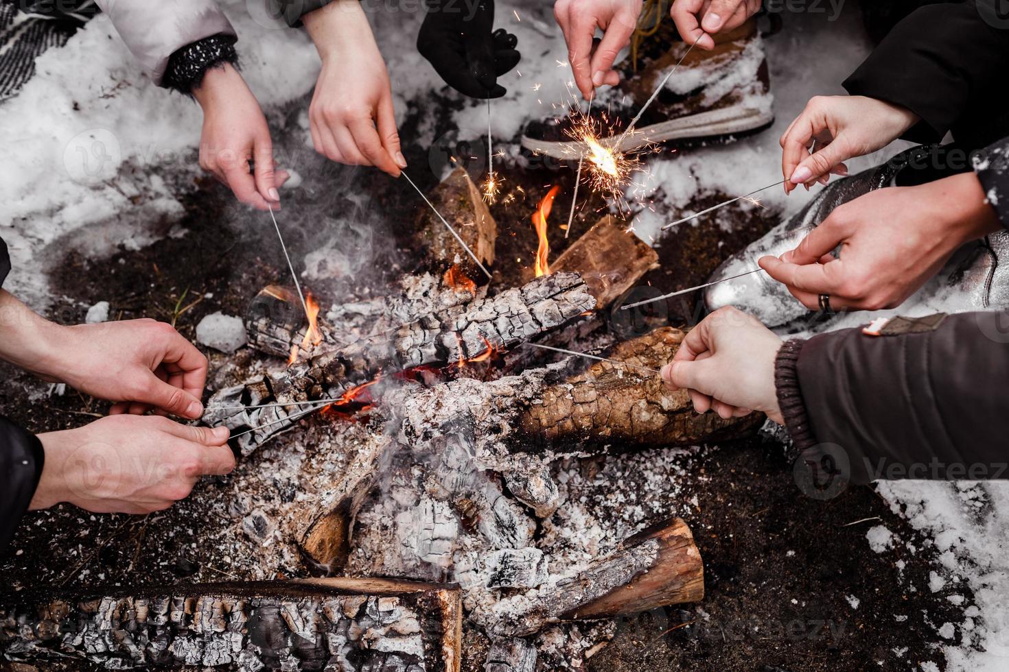 Young people sitting around campfire in the forest in winter and burning bengal lights. burn bonfire photo