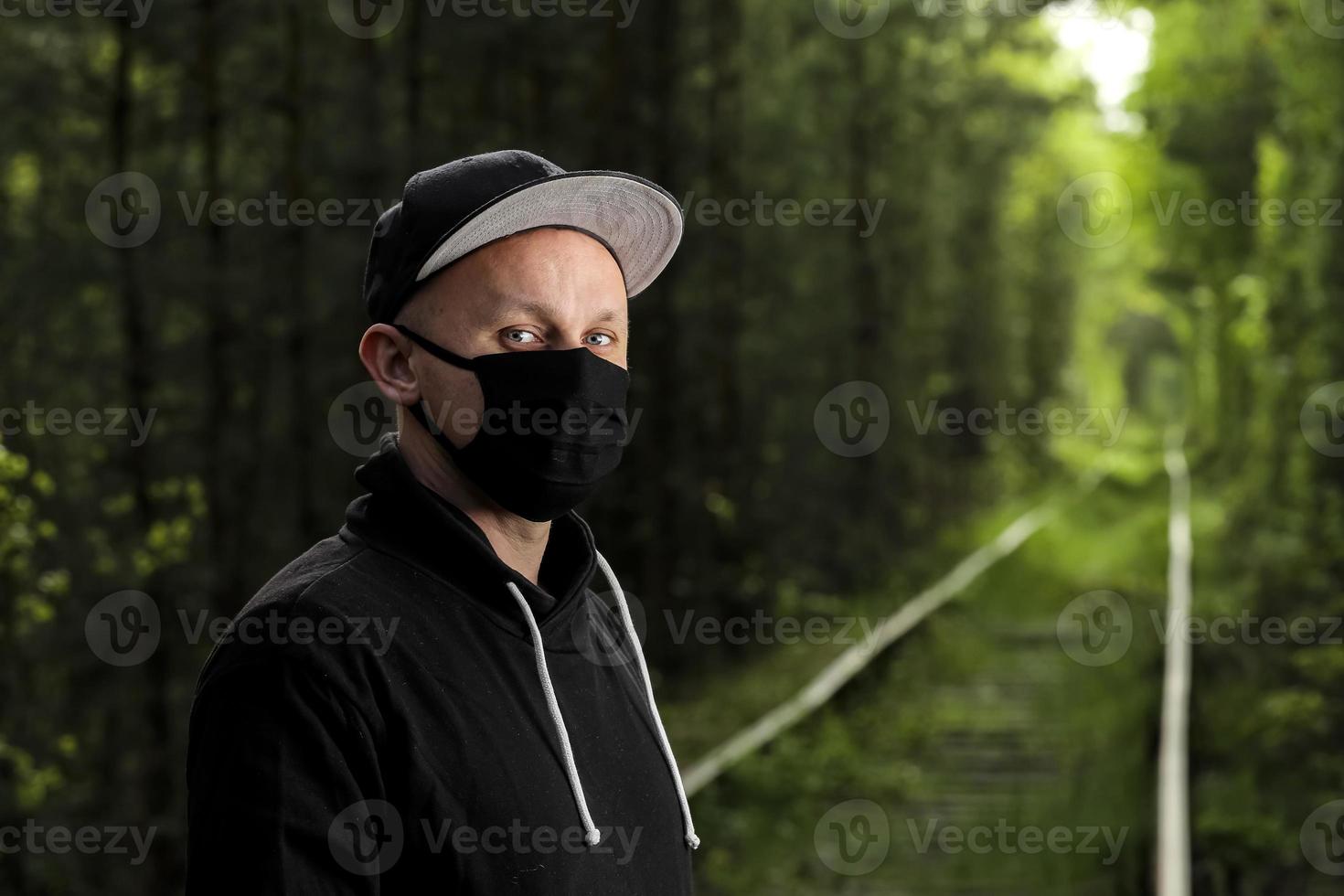 Young man in black protective antiviral mask in the summer park. The guy is resting outdoors on a sunny summer day in a mask made by his own hands. Virus protection. Quarantine measures photo