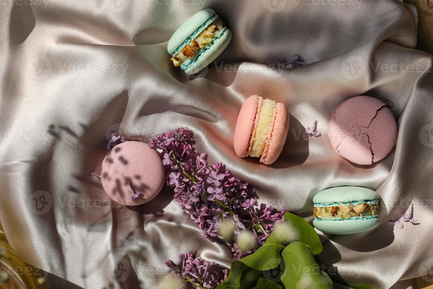 galletas de macarons o macarons franceses de rosa y menta y flores lilas sobre un fondo de tela. sabores naturales de frutas y bayas, relleno cremoso para el día de la madre de san valentín pascua con comida de amor foto