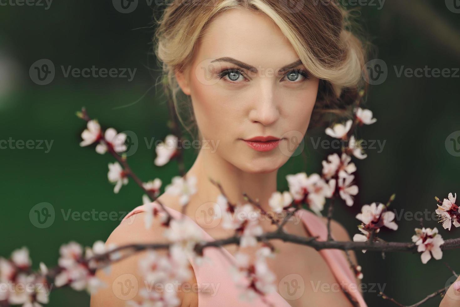 Portrait of young beautiful blonde woman in pink dress near blooming tree with white flowers on a sunny day. Spring, girl near a flowering tree photo