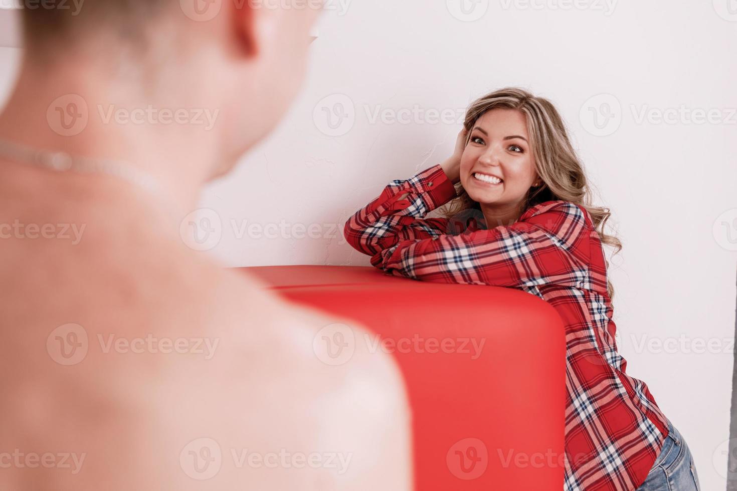 pareja joven sentada en la cama en una sala de estar y divirtiéndose juntos. él siempre la hace reír. jóvenes juguetones sonriendo y divirtiéndose mientras pasan tiempo libre en casa foto