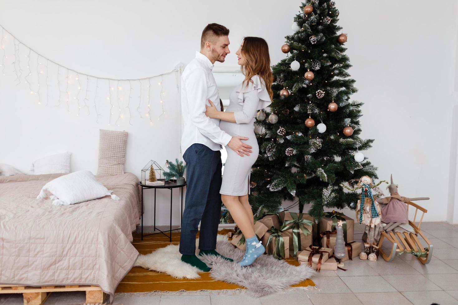 elegante hermosa pareja embarazada enamorada en navidad, descansando en las vacaciones de navidad antes del año nuevo. gran vientre embarazado. foto