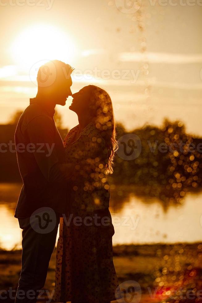 silueta de pareja amorosa abrazándose en el lago al atardecer. hermosa joven pareja enamorada caminando por la orilla del lago al atardecer en los rayos de luz brillante. copie el espacio enfoque selectivo foto