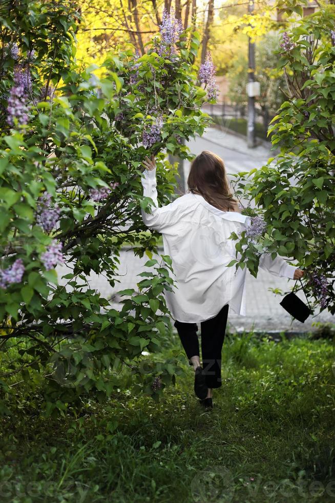 irreal impresionante hermosa mujer joven caminando en un verde florecido en primavera en un jardín de lavanda con un ramo de lilas en las manos. retrato romántico de moda de primer plano. oliendo las flores foto