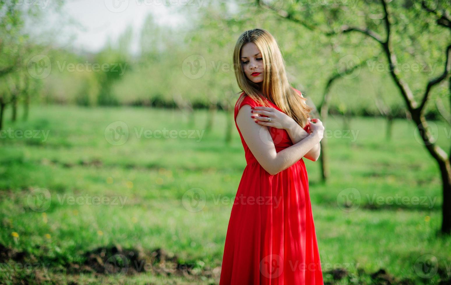 Portrait of light hair girl on red dress background spring garden. photo