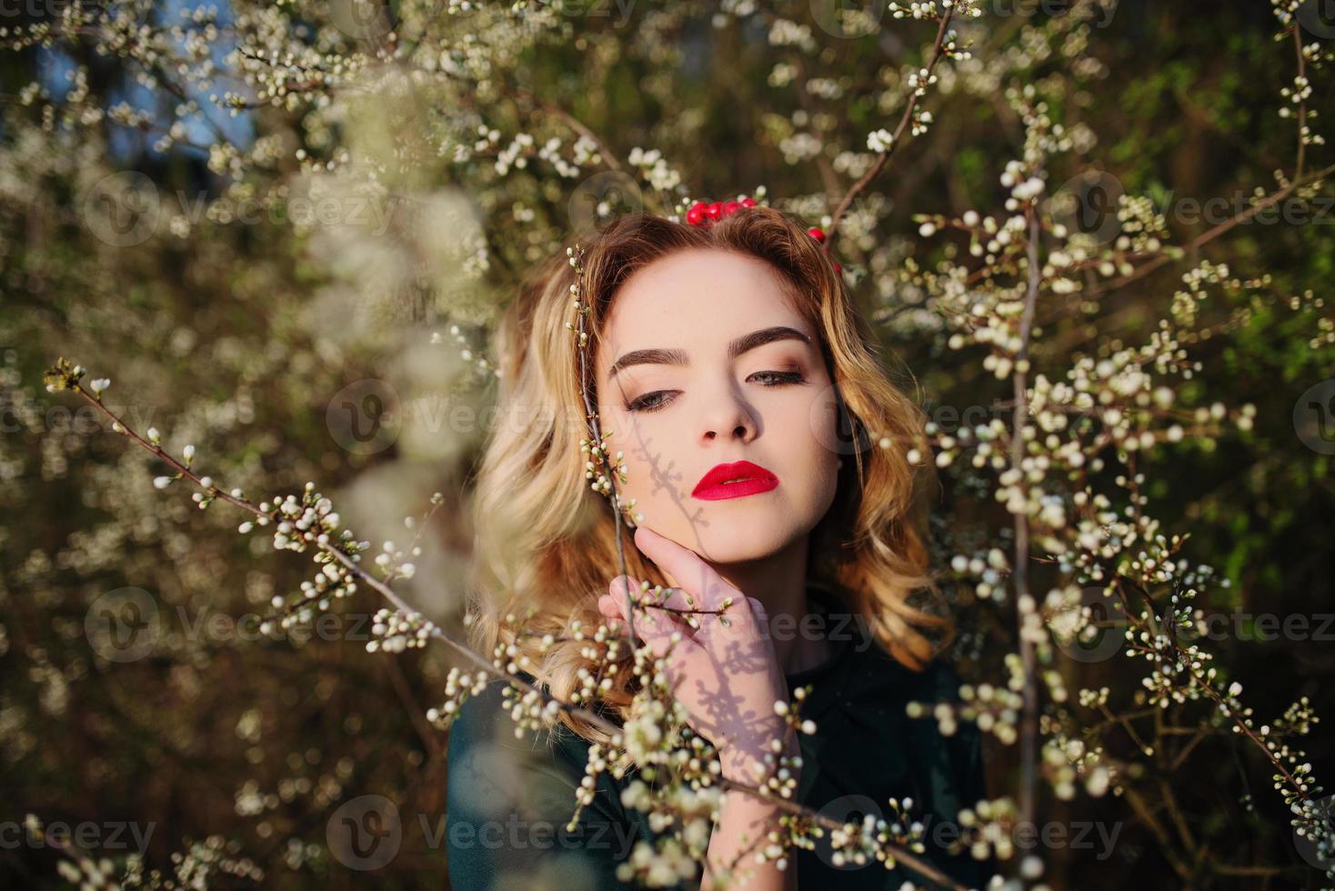 Close up portrait of yong elegance blonde girl at green dress on the garden in spring on blossom trees. photo