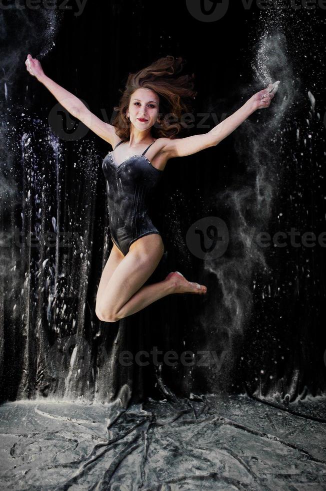 Girl dancer jumping and dancing in the white dust with flour on a black background. Studio shot of woman dancing with flour. photo