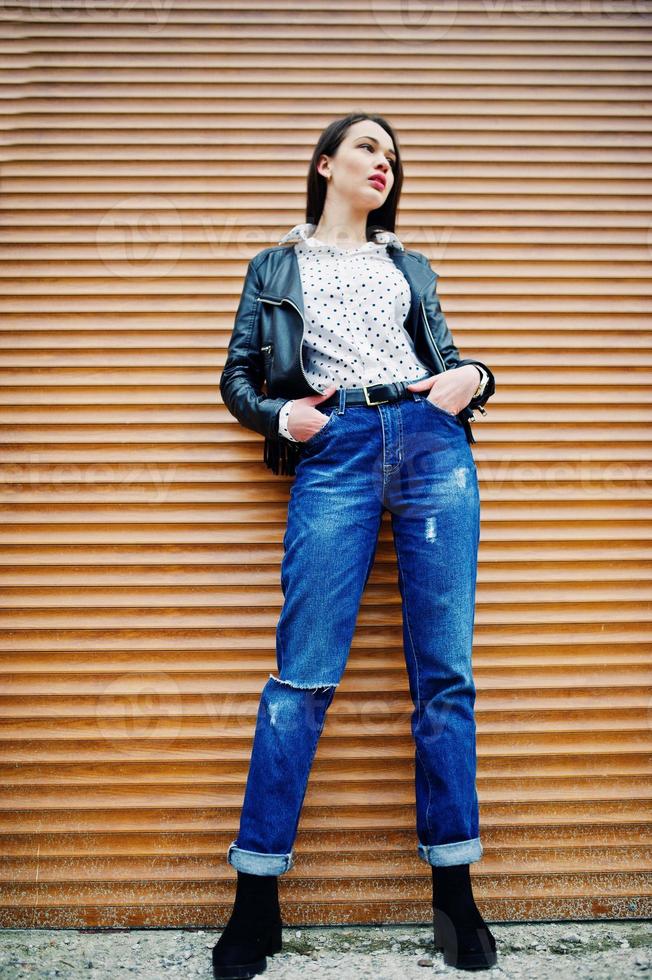 retrato completo de una joven elegante vestida con chaqueta de cuero y textura de obturador de fondo de jeans rasgados. estilo de modelo de moda callejera. foto