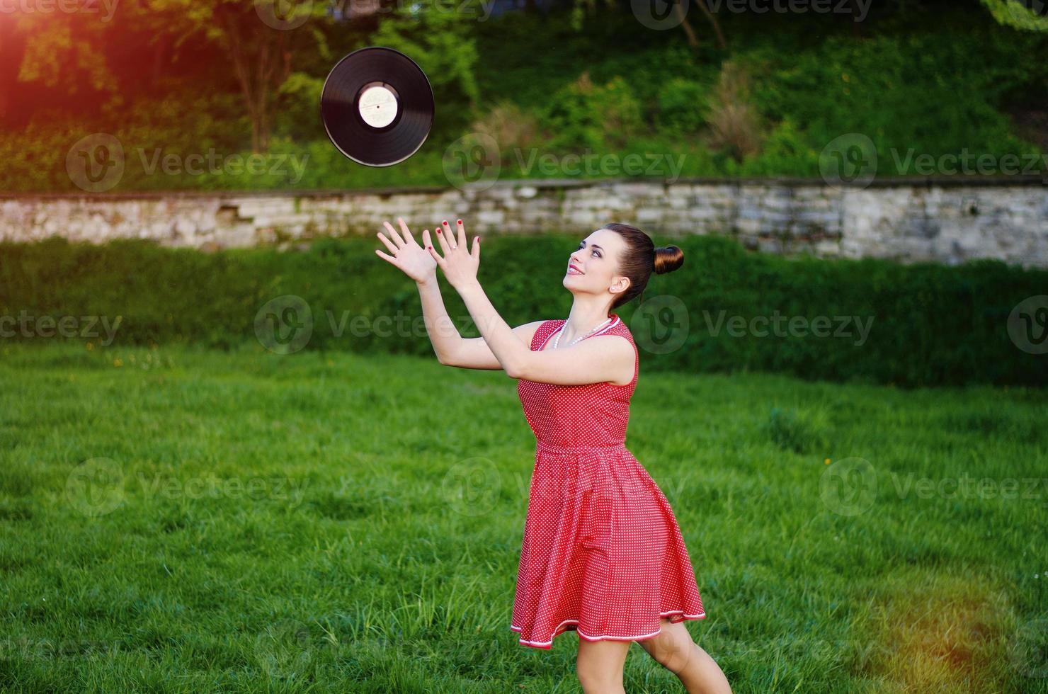 Portrait of young pinup girl wearing at retro vintage old-fashioned dress in peas with vinyl audio record, retro styling. photo