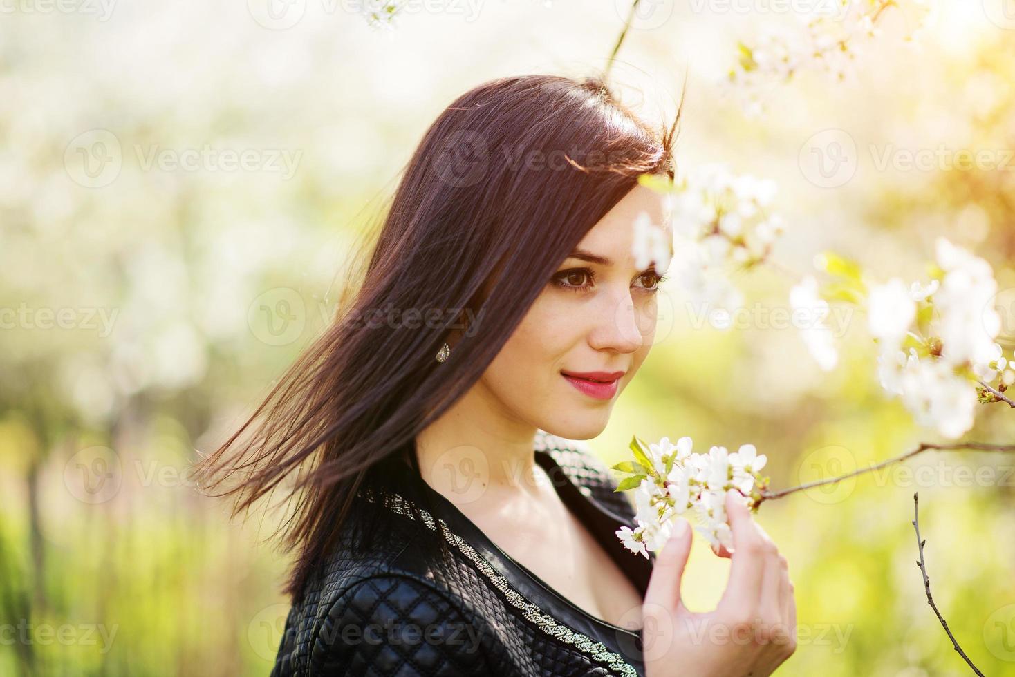 Close up portrait of young brunette girl with cherry blossom at spring garden. photo