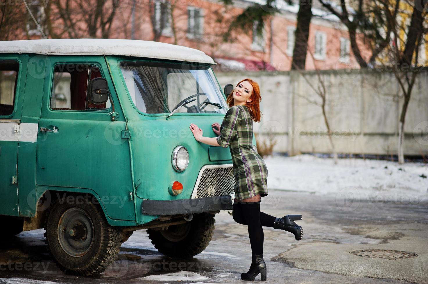 Young red haired girl posed on checkered dress background old retro cyan minivan. photo