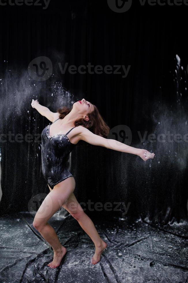 Girl dancer jumping and dancing in the white dust with flour on a black background. Studio shot of woman dancing with flour. photo