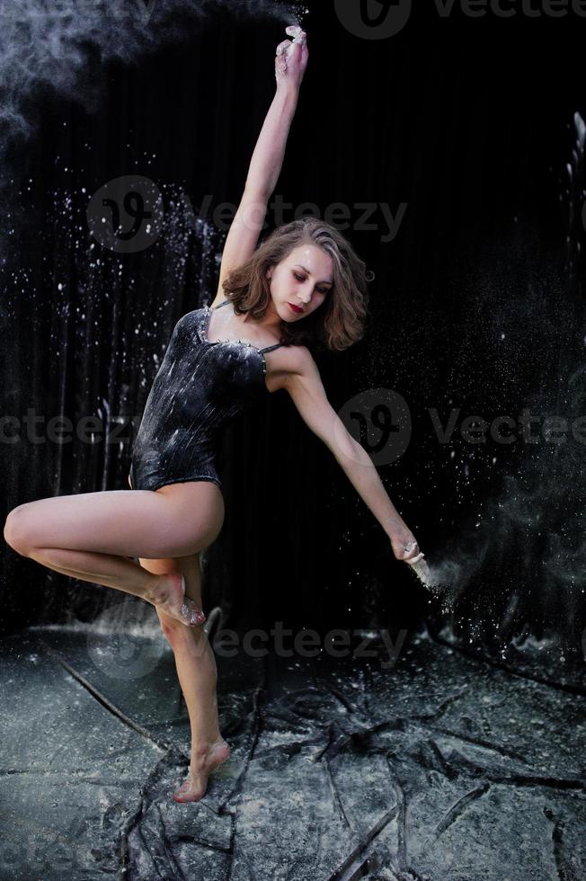 Girl dancer jumping and dancing in the white dust with flour on a black background. Studio shot of woman dancing with flour. photo