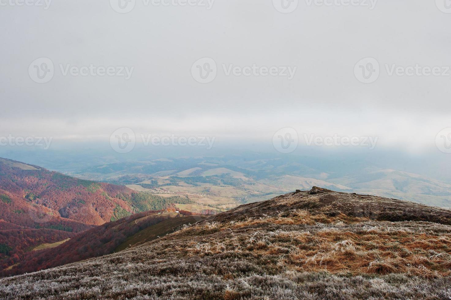 cima de la colina de la montaña helada en el fondo de las montañas de los cárpatos colina del bosque rojo de otoño. encuentro de otoño e invierno sobre la naturaleza. foto