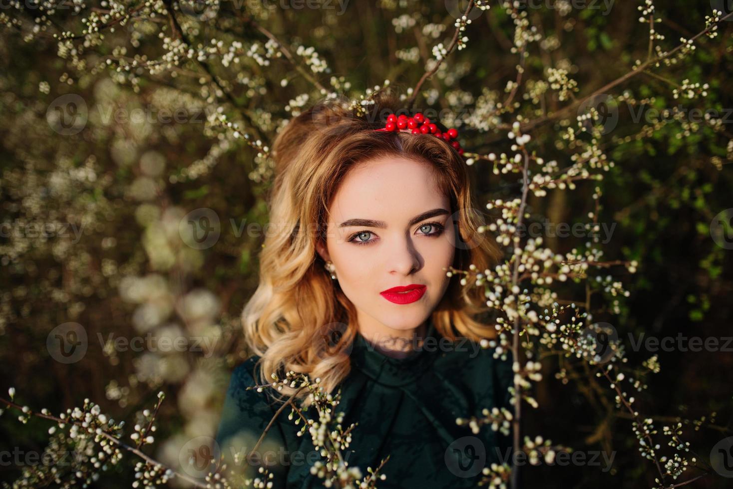 Close up portrait of yong elegance blonde girl at green dress on the garden in spring on blossom trees. photo